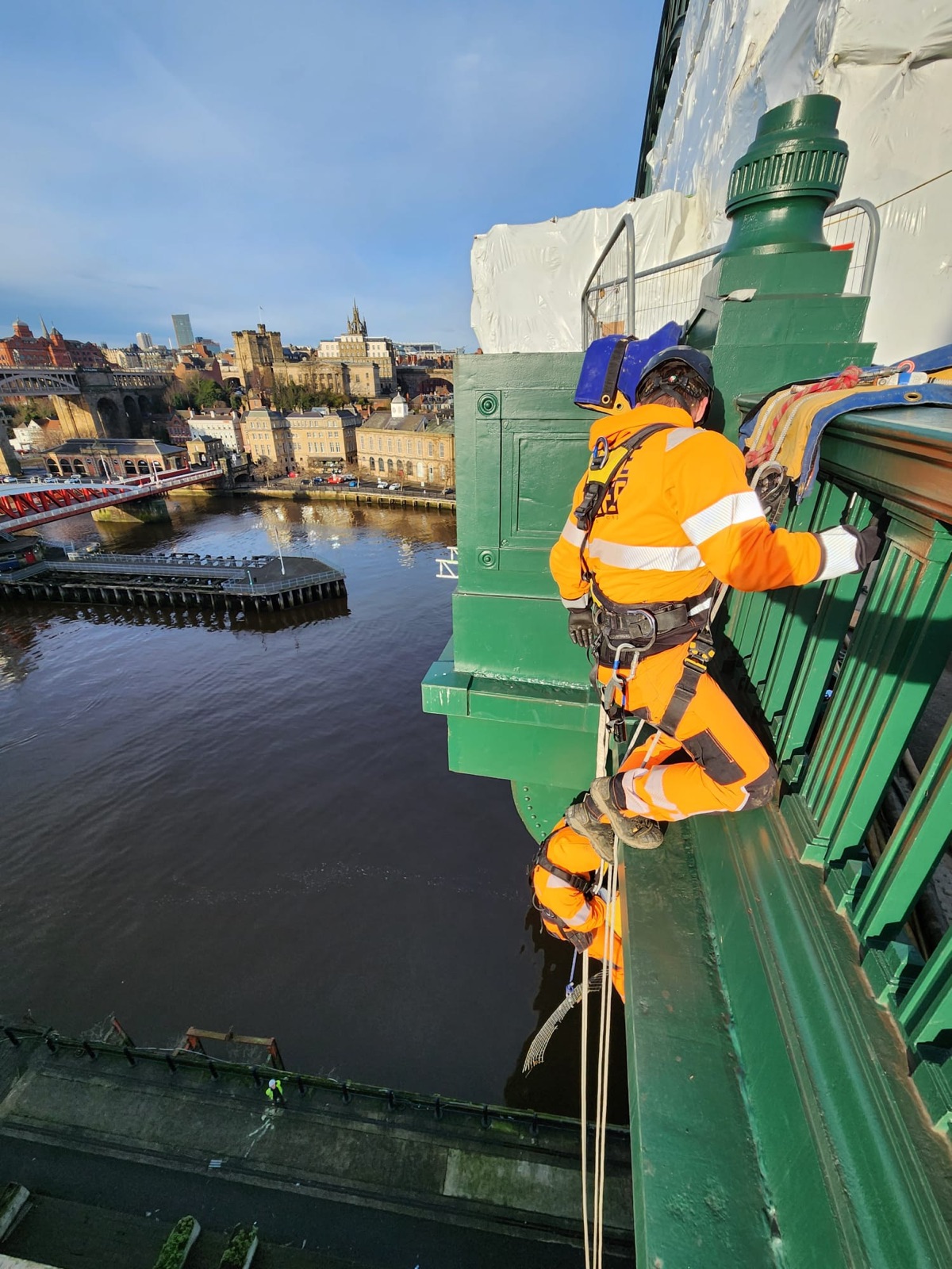 Technician on rope working on the side of a green steel bridge above a river