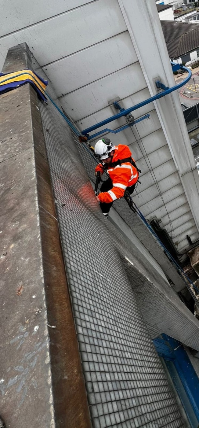 Technician on rope beside a tall brick stack