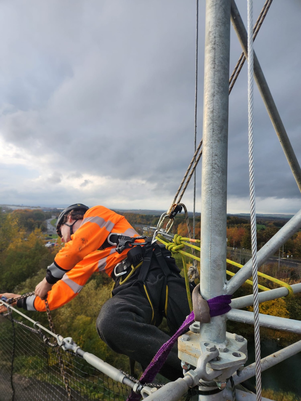 Technician climbing a steel mast with autumn trees below